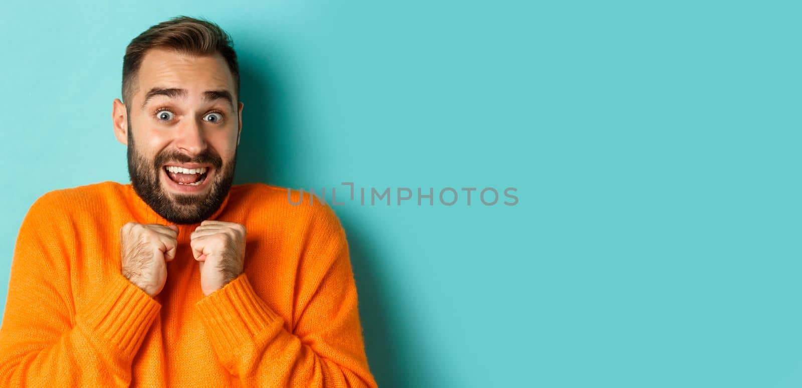 Close-up of startled man gasping and pressing hands to chest, staring at camera shocked, standing over light blue background.