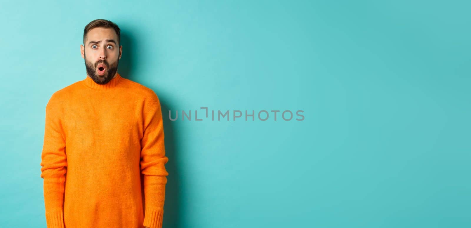 Shocked and confused man looking in awe at promo offer, standing near copy space on turquoise background by Benzoix