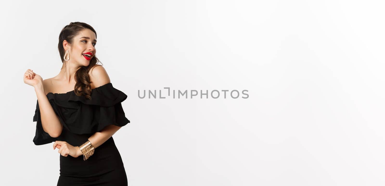 Fashion and beauty. Woman celebrating and dancing in black dress, having fun and smiling, standing over white background.