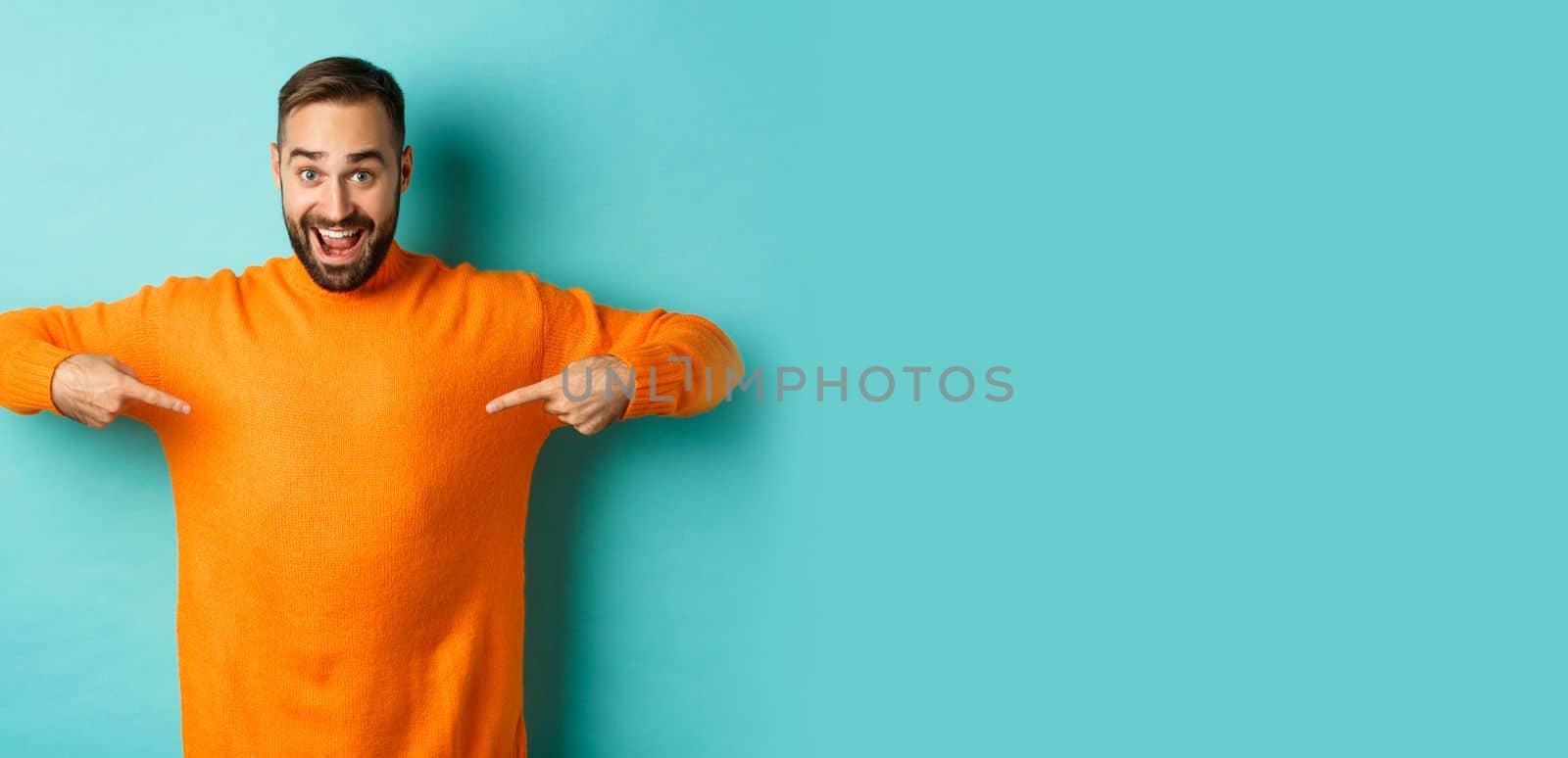 Happy man pointing at sweater, showing your logo banner on clothes, standing over light blue background.