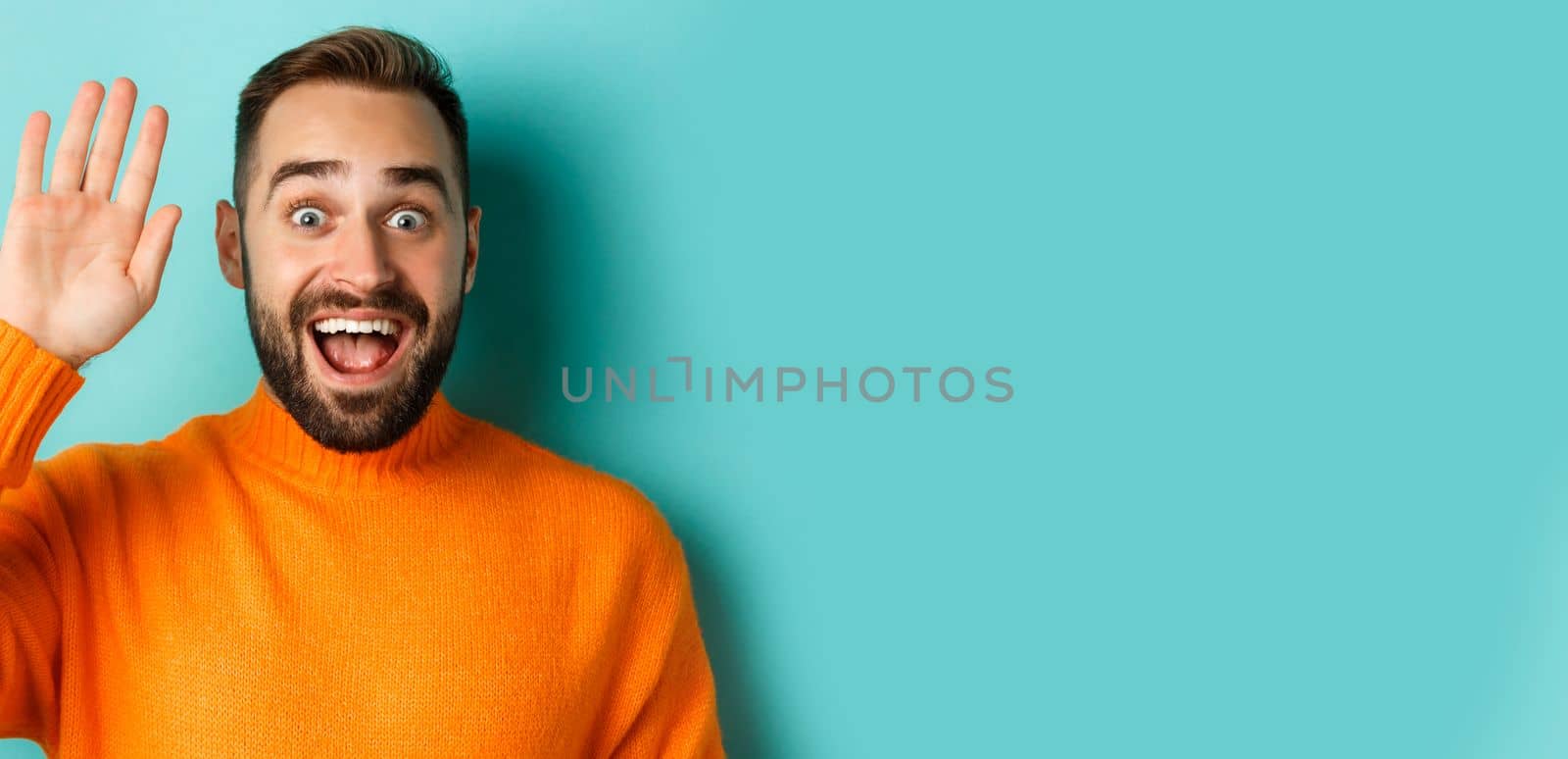 Handsome man waving hand to say hello, giving high five, standing over light blue background.