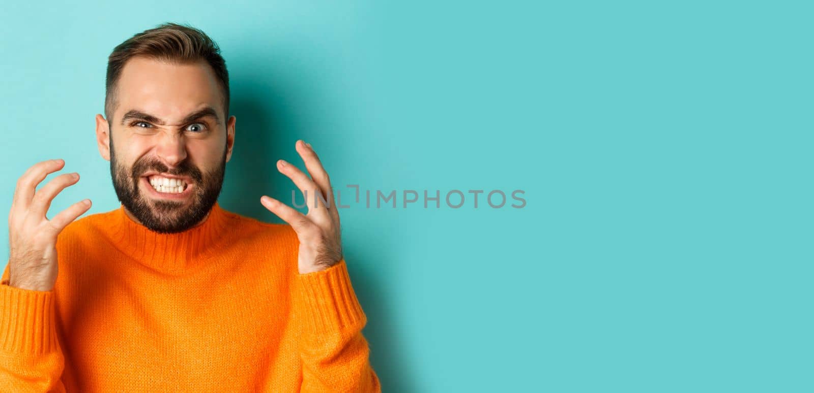 Close-up of angry caucasian man looking mad, grimacing and shaking hands, having break down, standing over light blue background.