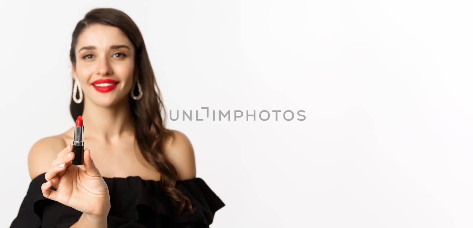 Fashion and beauty concept. Beautiful woman in black dress showing red lipstick and smiling, standing over white background.