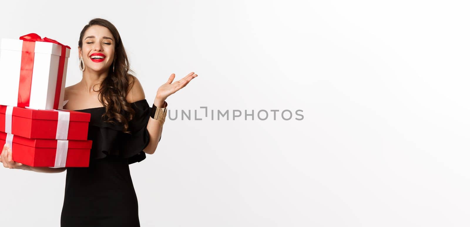 Celebration and christmas holidays concept. Excited and happy woman receive gifts, holding xmas presents and rejoicing, standing in black dress over white background by Benzoix