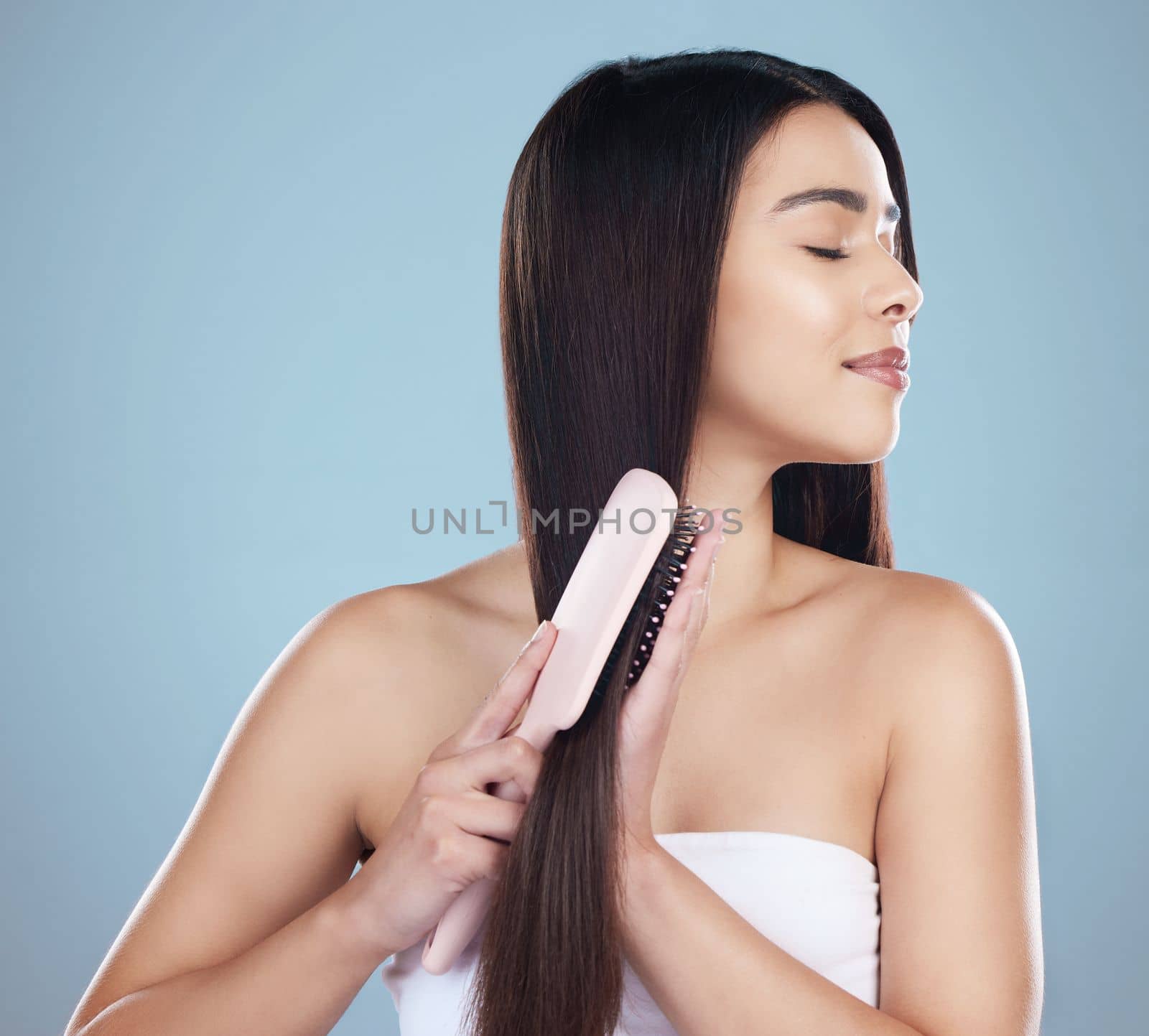 Ah, that silky glide. Studio shot of a beautiful young woman brushing her long silky hair while posing against a blue background. by YuriArcurs