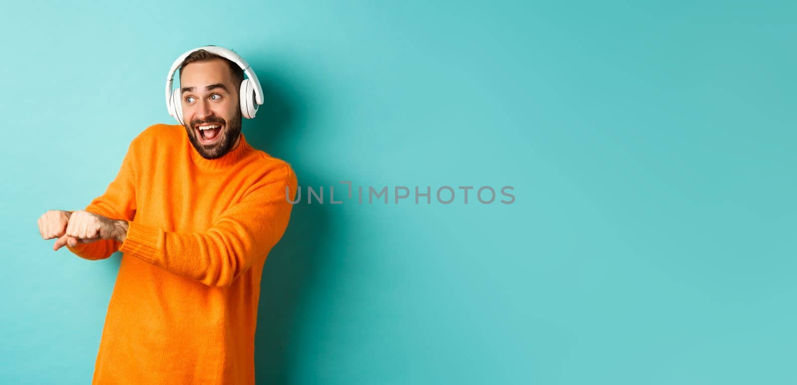 Happy man listening music in headphones and dancing funny, standing over turquoise background by Benzoix