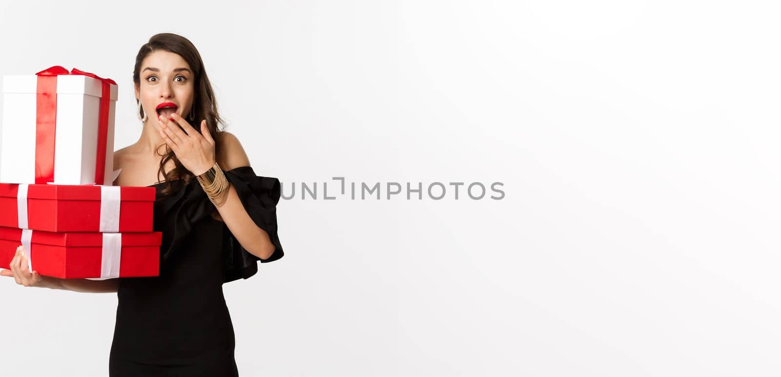 Celebration and christmas holidays concept. Woman holding xmas gifts and looking surprised, receive presents, standing over white background.