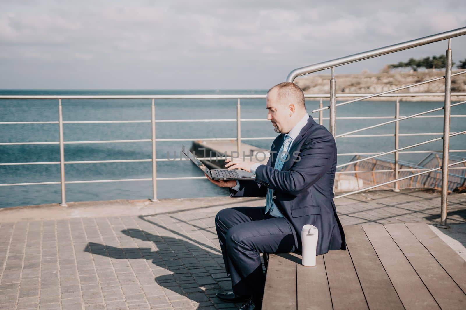 Digital Nomad, a young tattooed man working remotely online, typing on a laptop keyboard while sitting on a beach at sunset. Working remotely on vacation, running an online business from a distance