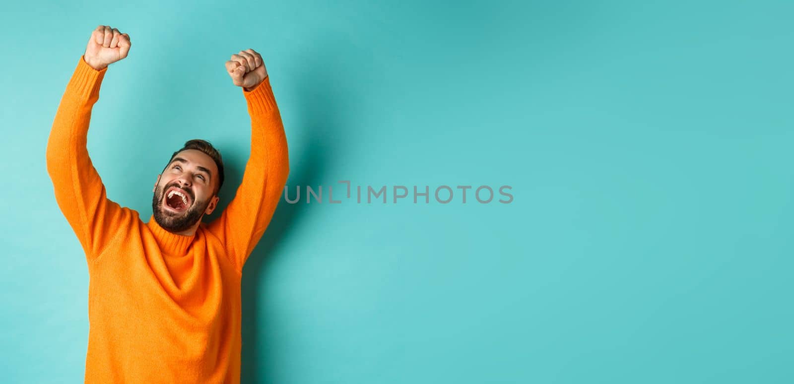 Happy man triumphing and feeling rejoice of winning, celebrating victory, standing over light blue background. Copy space