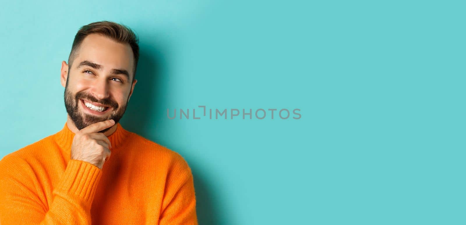 Close-up of caucasian male model having an idea, smiling and looking upper left corner thoughtful, imaging plan, standing over light blue background by Benzoix