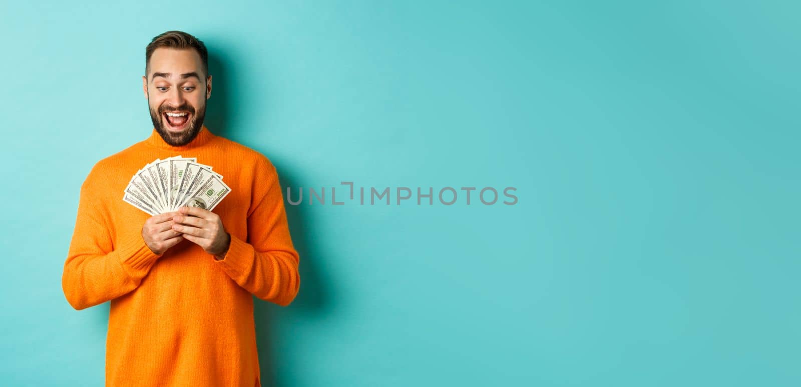 Image of man looking happy at money, smiling amazed, standing over light blue background by Benzoix