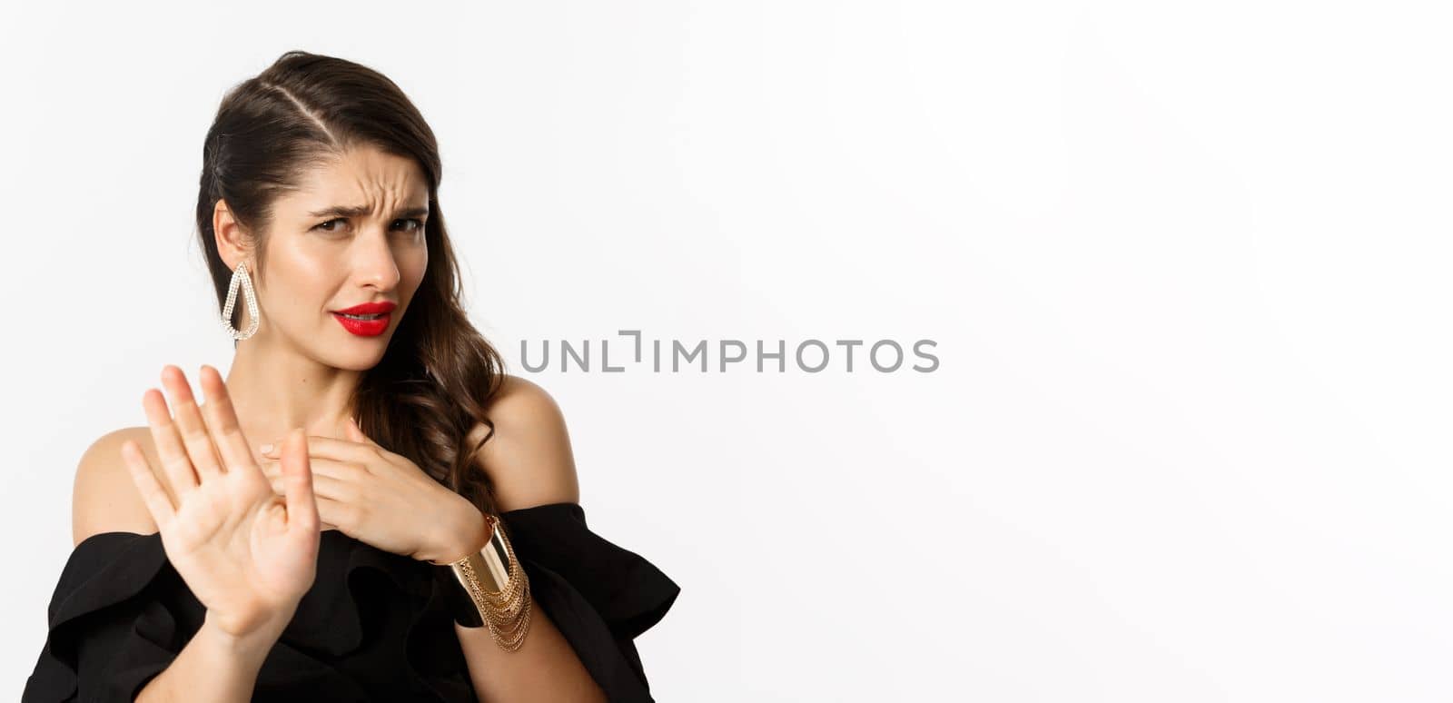 Fashion and beauty concept. Close-up of displeased young woman in black dress saying no, declining offer and looking with disdain, standing over white background.