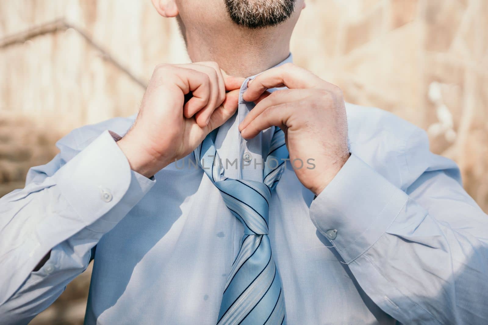 Close up of Man Adjusting Tie of Suit. Businessman in blue shirt straightens his tie, close-up by panophotograph