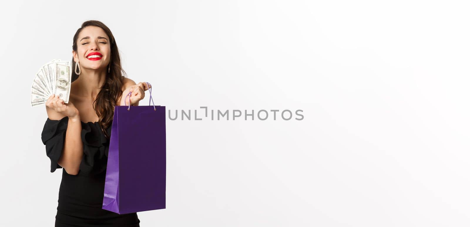 Satisfied and happy woman enjoying shopping, holding bag and money, smiling pleased, standing over white background.