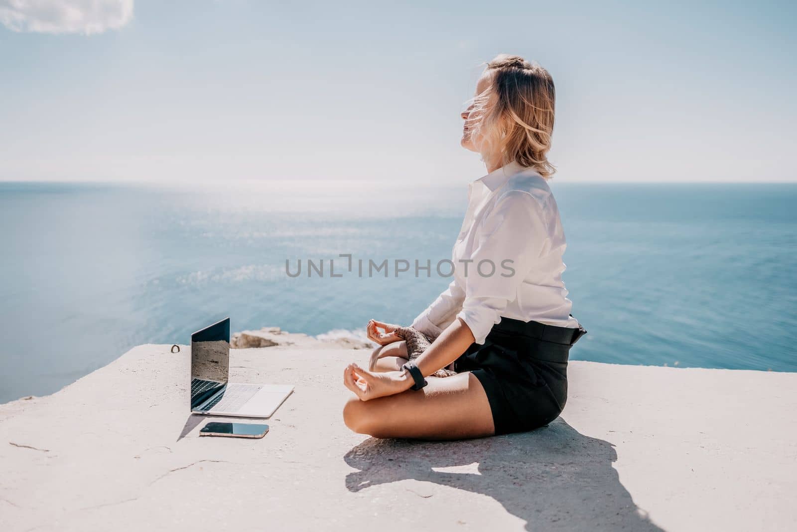 Happy girl doing yoga with laptop working at the beach. beautiful and calm business woman sitting with a laptop in a summer cafe in the lotus position meditating and relaxing. freelance girl remote work beach paradise