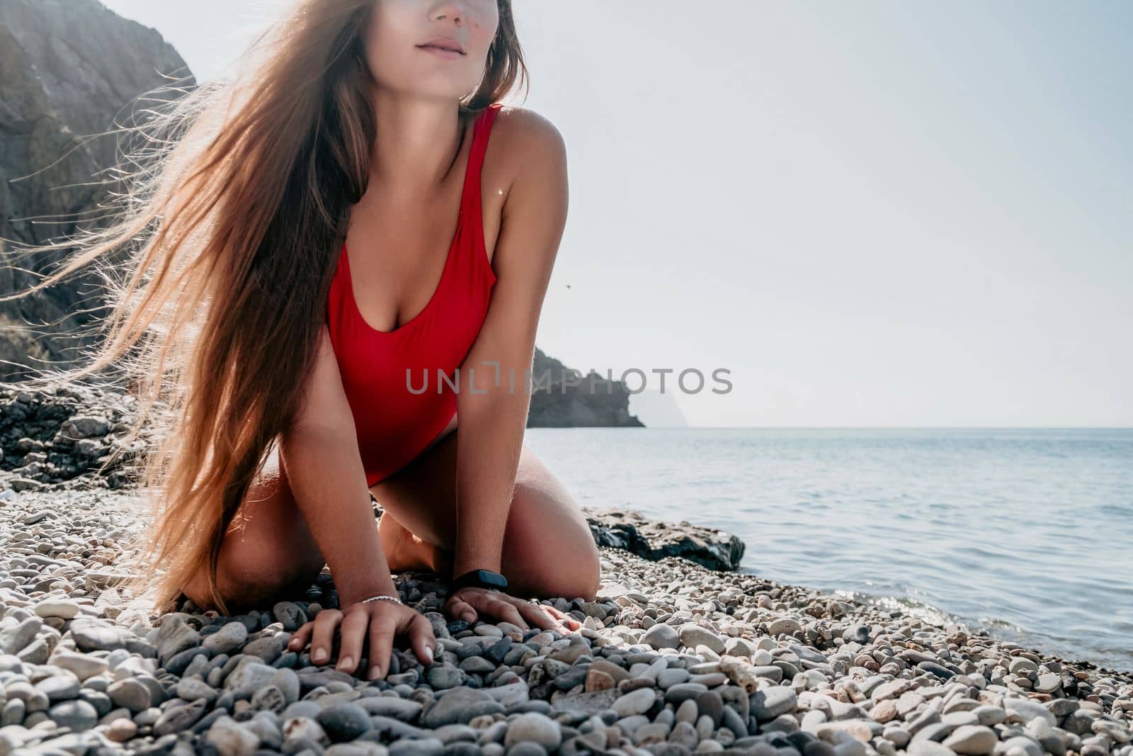 Young woman in red bikini on Beach. Girl lying on pebble beach and enjoying sun. Happy lady with long hair in bathing suit chilling and sunbathing by turquoise sea ocean on hot summer day. Close up by panophotograph