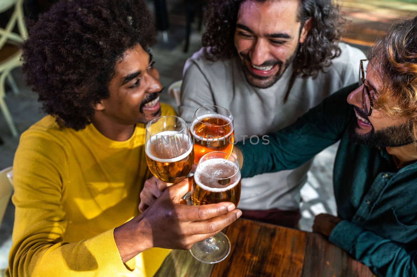 High angle view of happy male friends in a bar enjoying drinks together toasting with beer, having fun. by Hoverstock