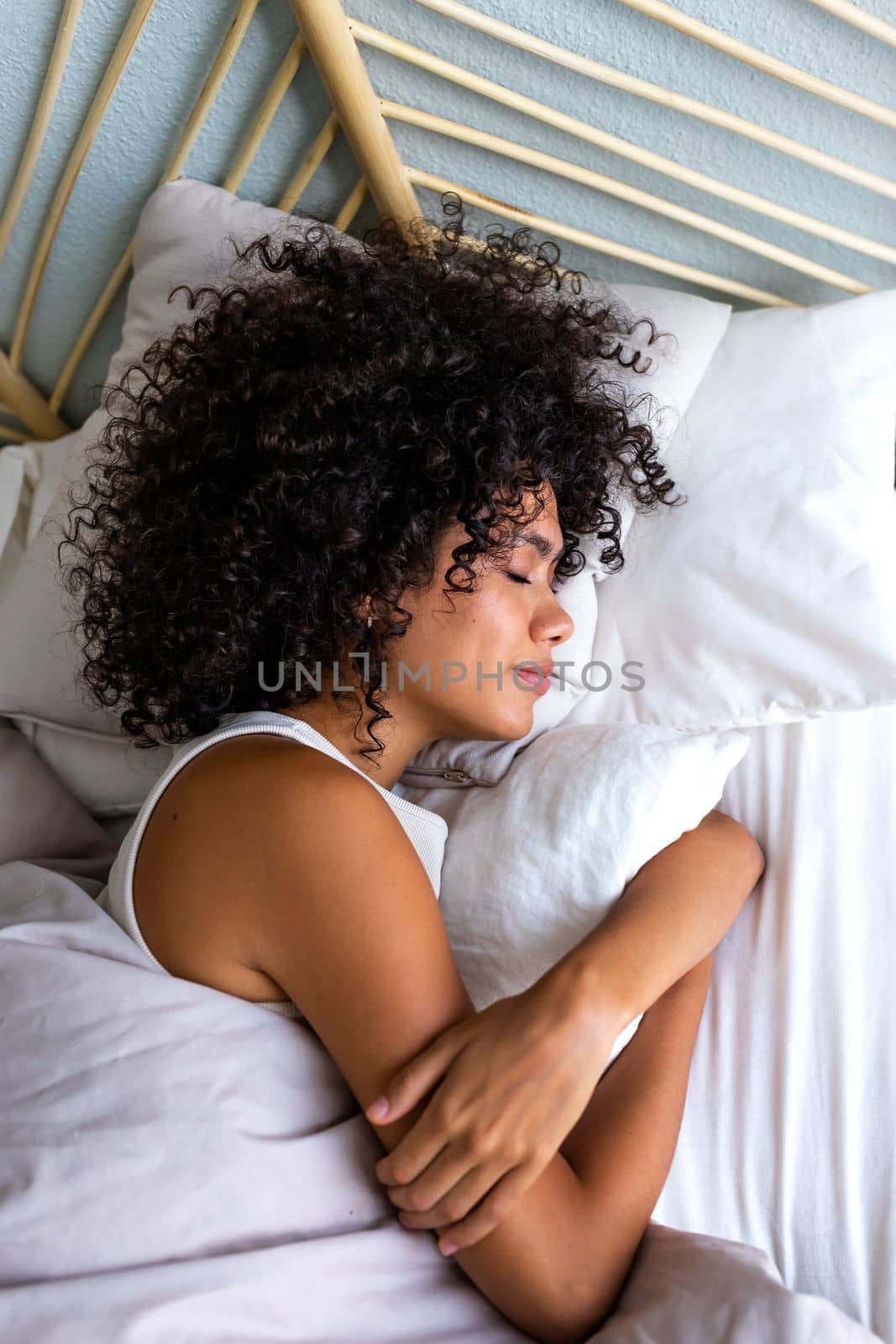Top view of calm and serene young multiracial woman with curly hair sleeping in bed at home cozy bedroom. Vertical by Hoverstock