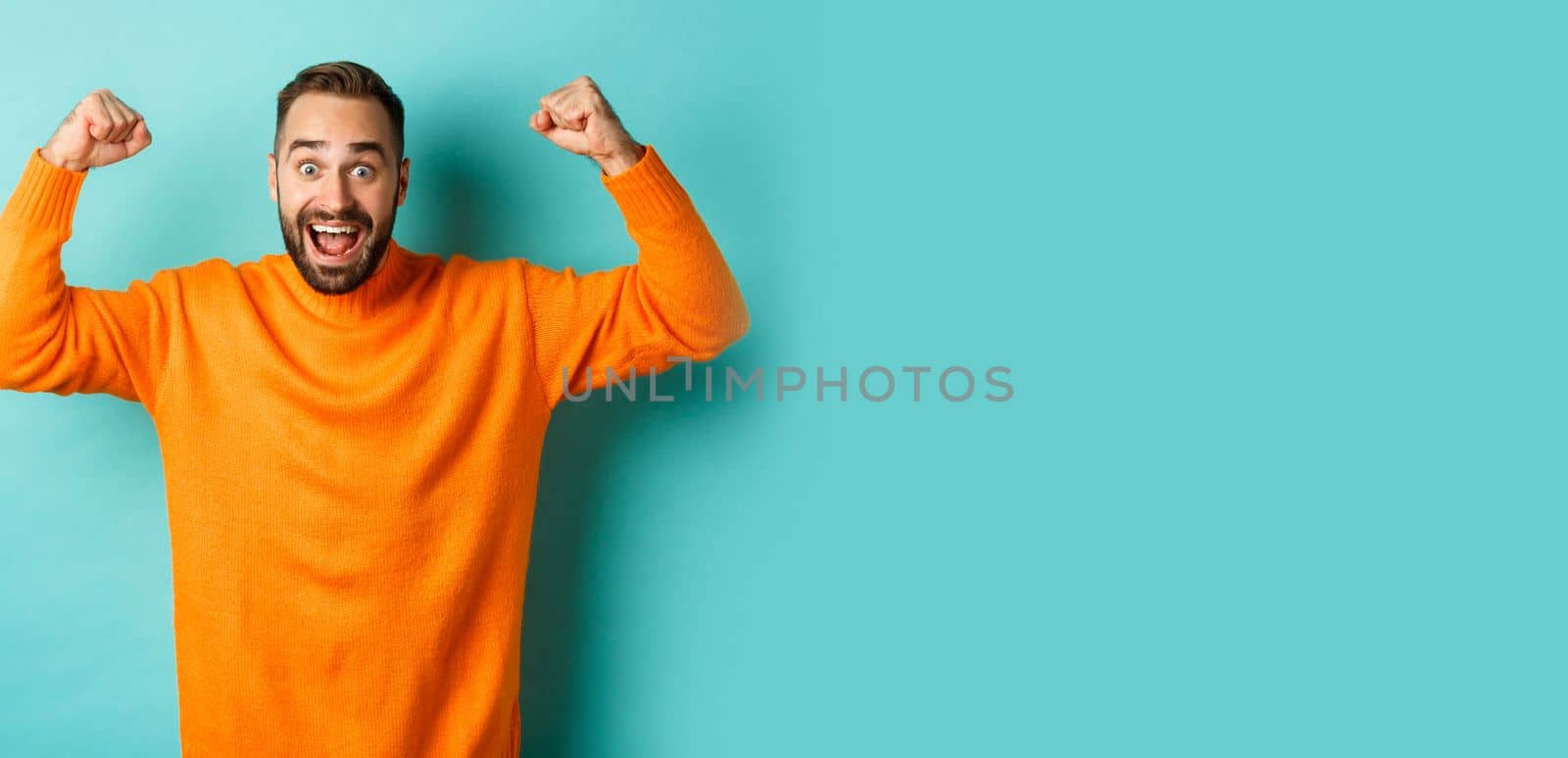 Handsome man celebrating victory, winning and looking happy, triumphing over win, standing over light blue background by Benzoix