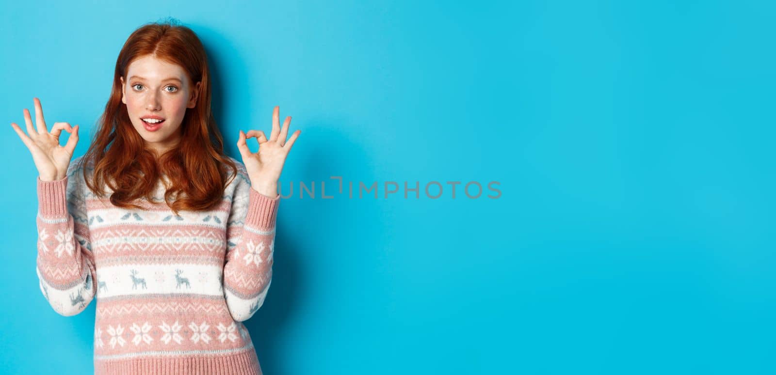 Image of young confident redhead woman showing okay signs, assure all good, praising choice, standing over blue background by Benzoix