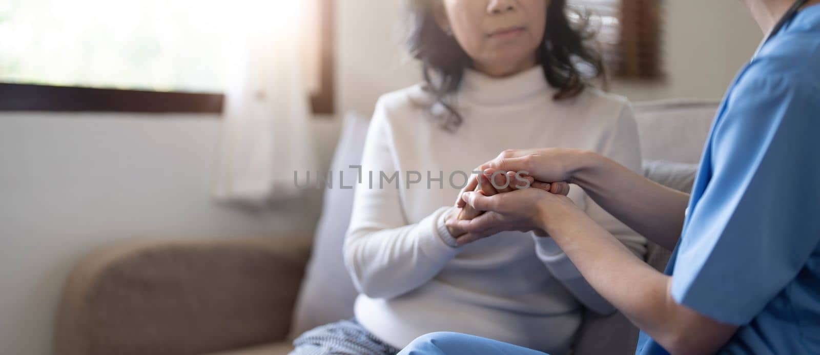 Happy patient is holding caregiver for a hand while spending time together. Elderly woman in nursing home and nurse