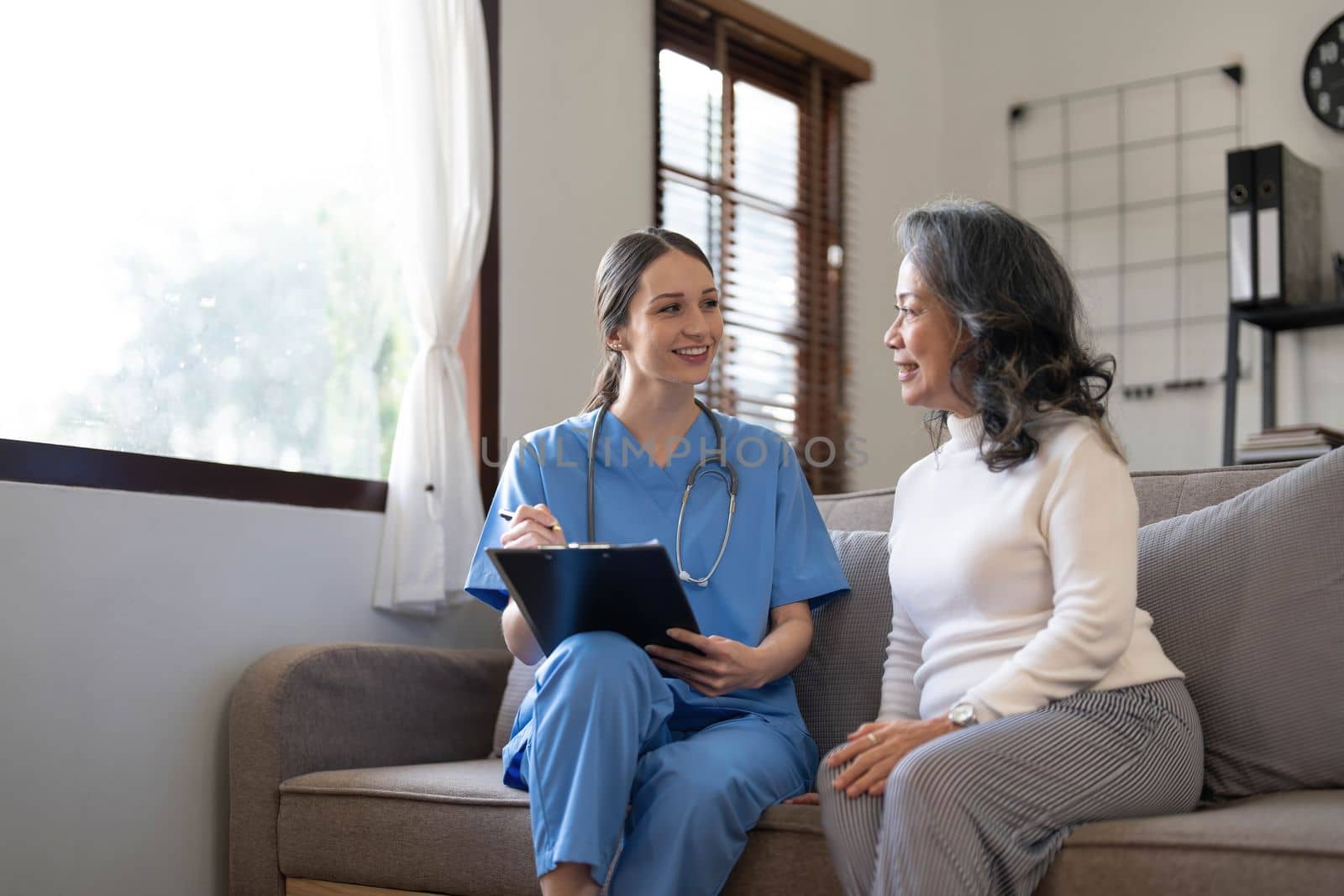 Asian nurse showing health checkup report to grandmather and giving advice. medical assisted living visit senior patient at home. Home nursing and healthcare caregiver concept..