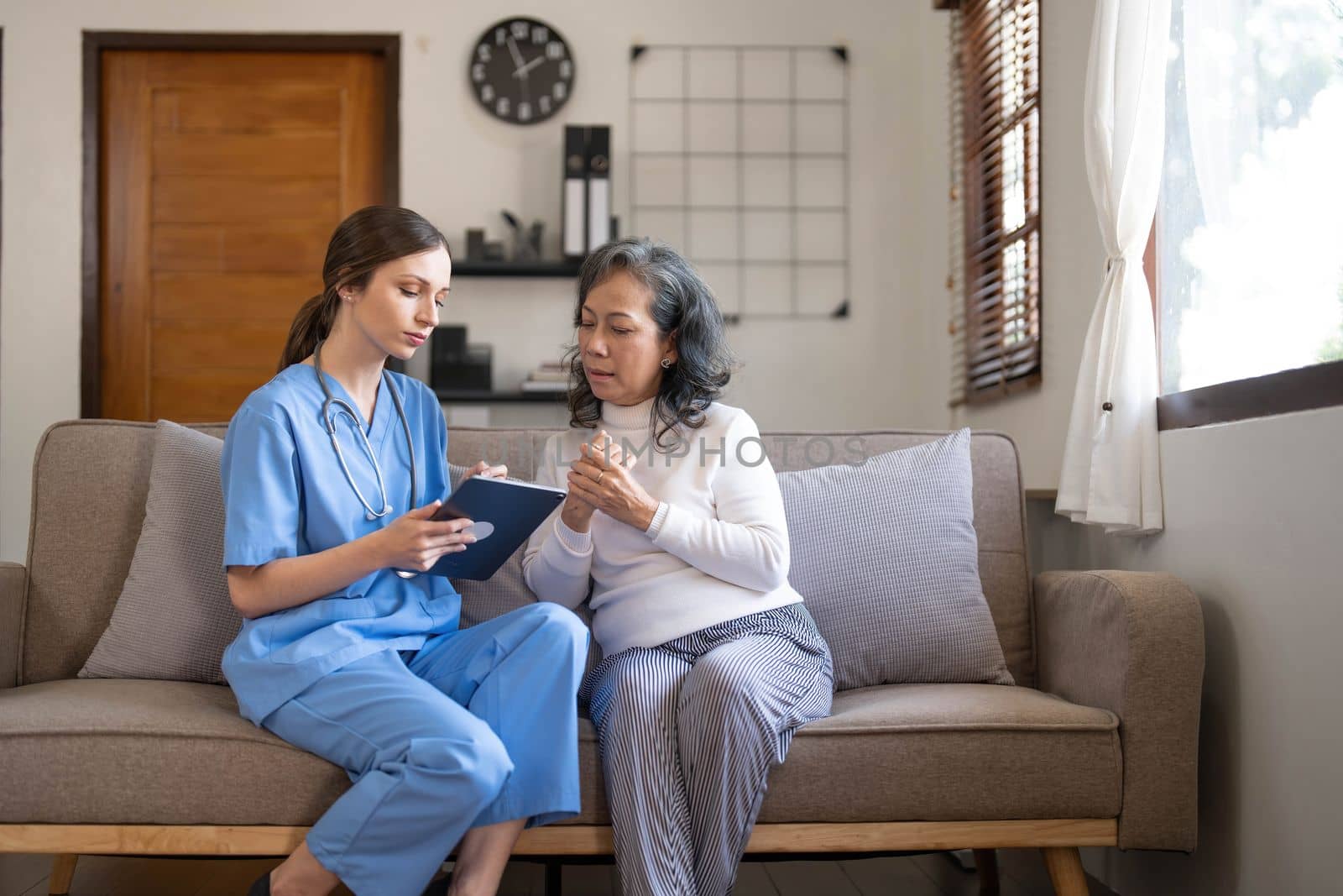 Asian nurse showing health checkup report to grandmather and giving advice. medical assisted living visit senior patient at home. Home nursing and healthcare caregiver concept by wichayada