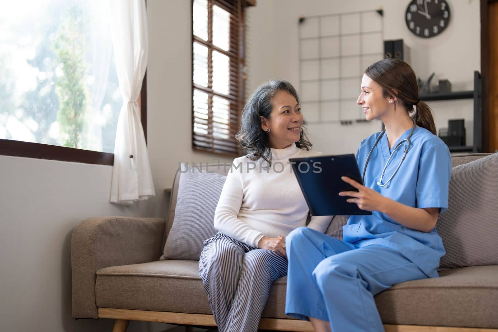 Asian nurse showing health checkup report to grandmather and giving advice. medical assisted living visit senior patient at home. Home nursing and healthcare caregiver concept by wichayada