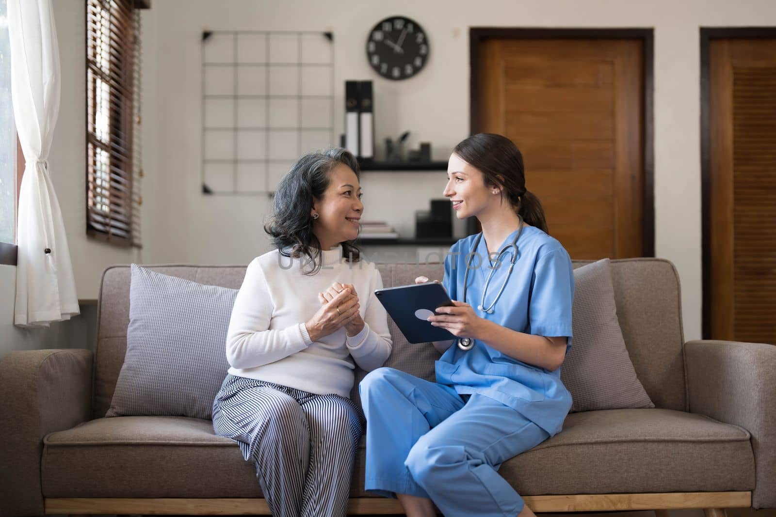 Asian nurse showing health checkup report to grandmather and giving advice. medical assisted living visit senior patient at home. Home nursing and healthcare caregiver concept..