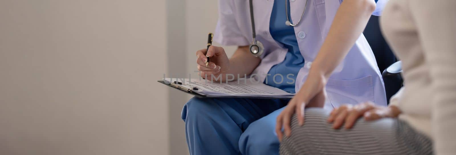 Asian female patient undergoing health check up while female doctor uses stethoscope to check heart rate in nurse, health care concept..