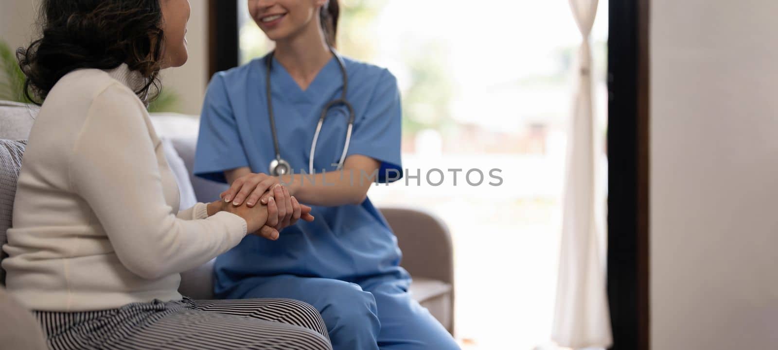 Happy patient is holding caregiver for a hand while spending time together. Elderly woman in nursing home and nurse...