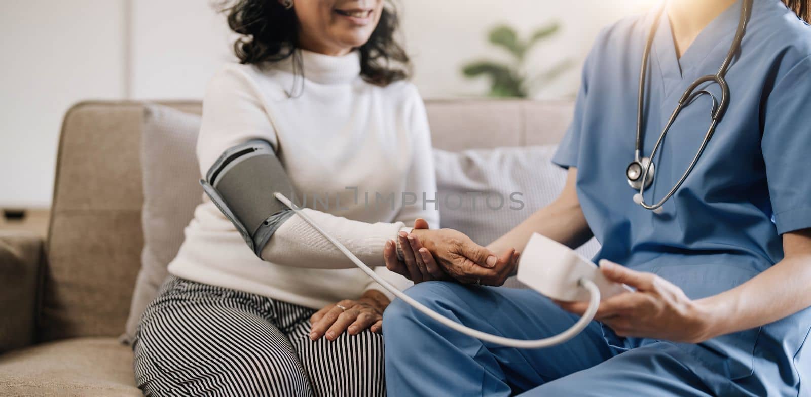 Happy senior woman having her blood pressure measured in a nursing home by her caregiver. Happy nurse measuring blood pressure of a senior woman in living room by wichayada