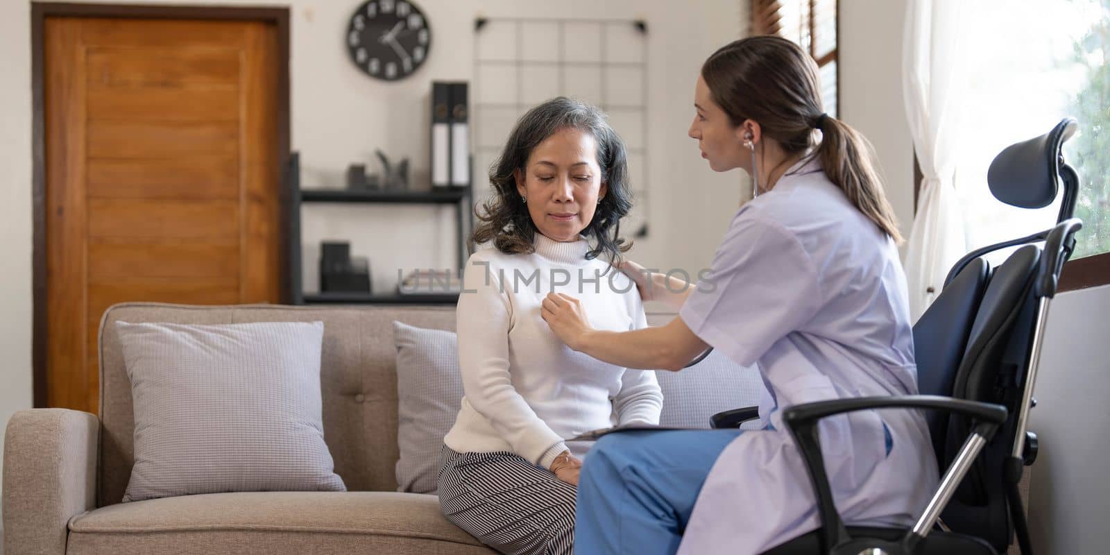 Asian female patient undergoing health check up while female doctor uses stethoscope to check heart rate in nurse, health care concept by wichayada