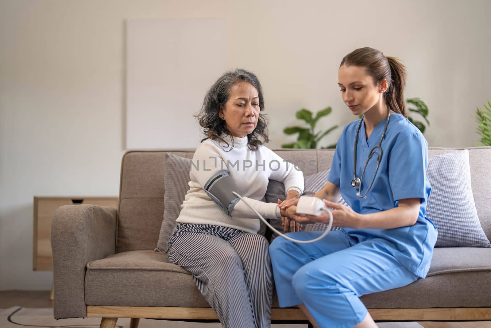 Happy senior woman having her blood pressure measured in a nursing home by her caregiver. Happy nurse measuring blood pressure of a senior woman in living room by wichayada