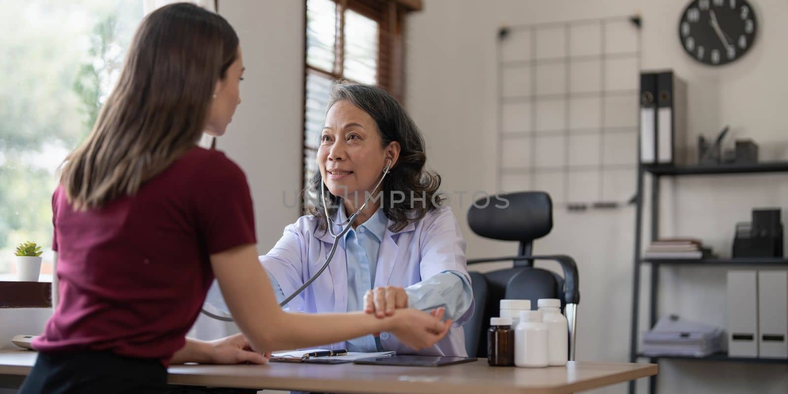 Middle aged female pediatrician listening to young woman's complaints with health problems And write down on the medical history paper during the treatment. health concept by wichayada