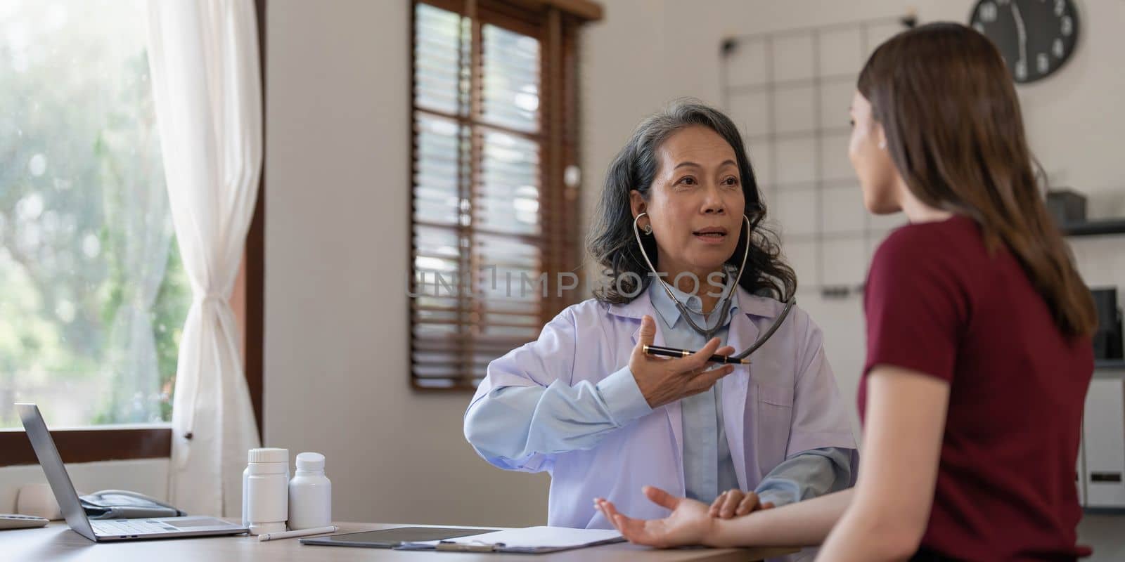 Middle aged female pediatrician listening to young woman's complaints with health problems And write down on the medical history paper during the treatment. health concept by wichayada