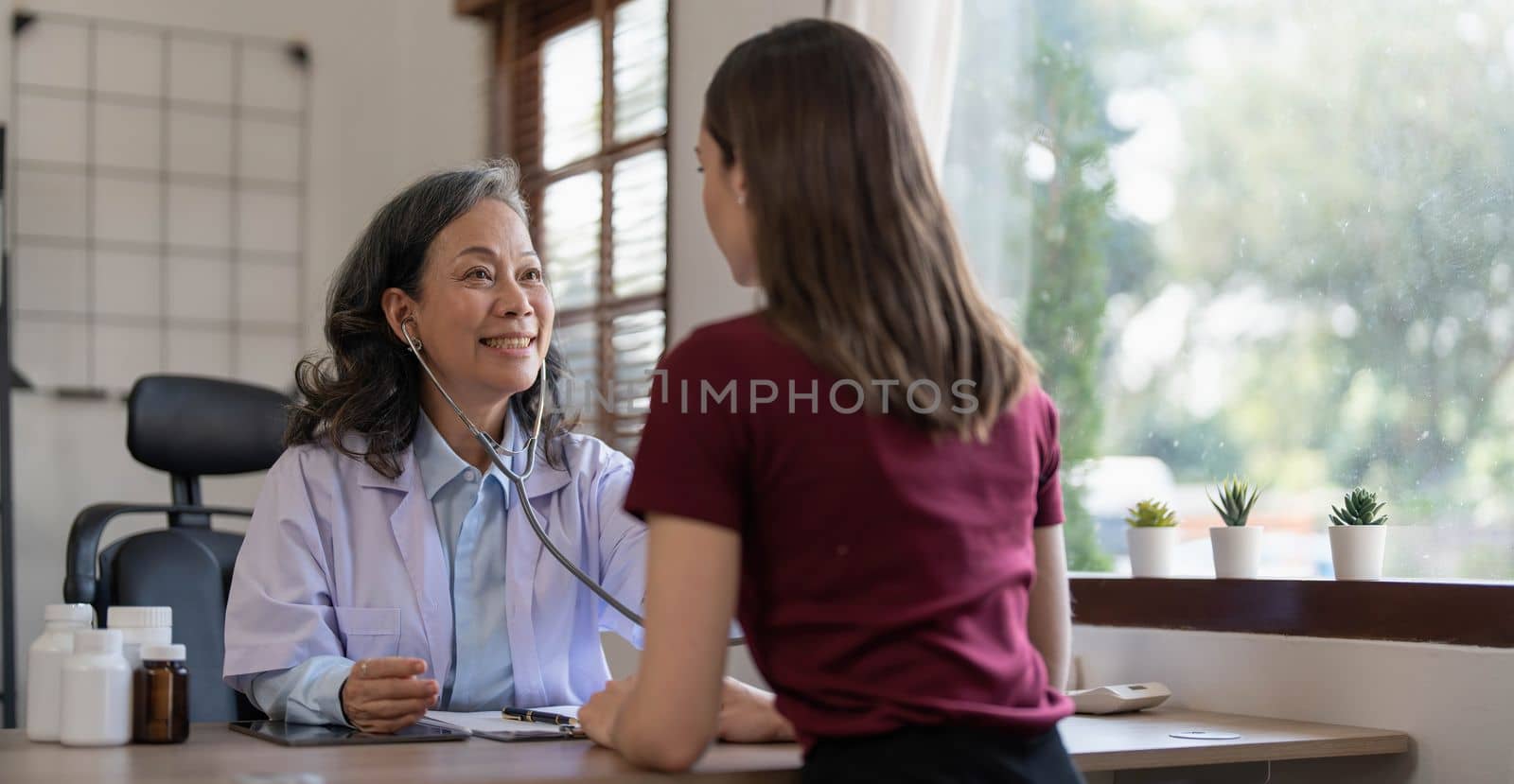 Middle aged female pediatrician listening to young woman's complaints with health problems And write down on the medical history paper during the treatment. health concept by wichayada