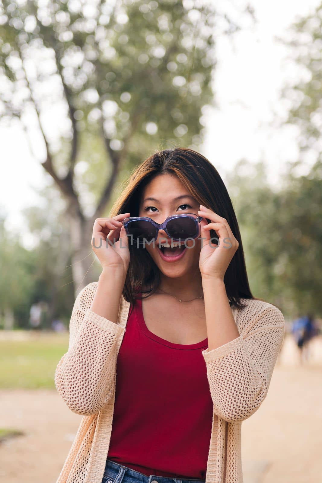 vertical portrait of a cheerful asian woman looking happy over her sunglasses, concept of youth and beauty