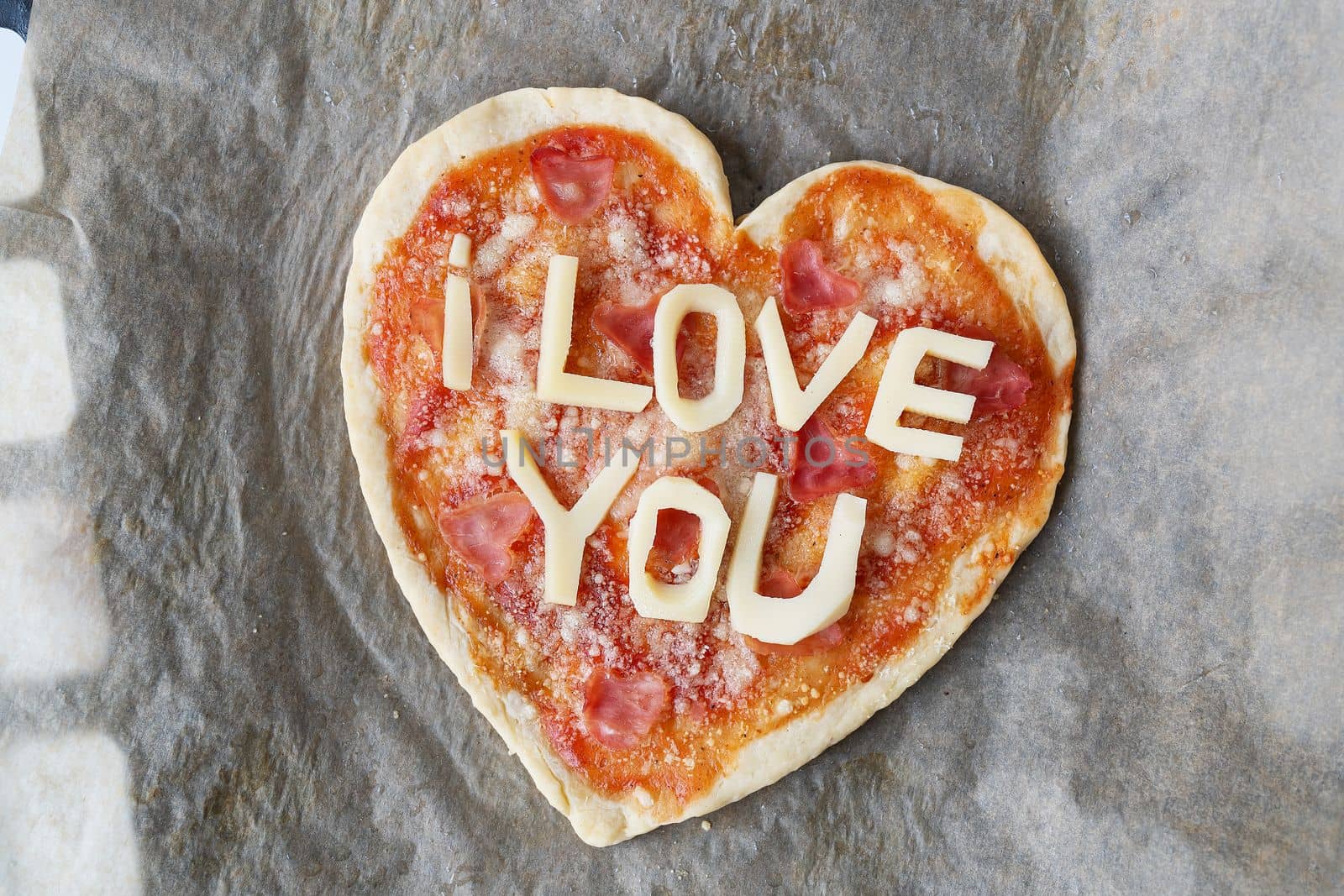 Italian heart shaped pizza with salami, tomato sauce, parmesan, pizza sauce, mozzarella and olive oil on parchment paper with cheese I love you. Love concept for Valentine's Day February 14. by sfinks