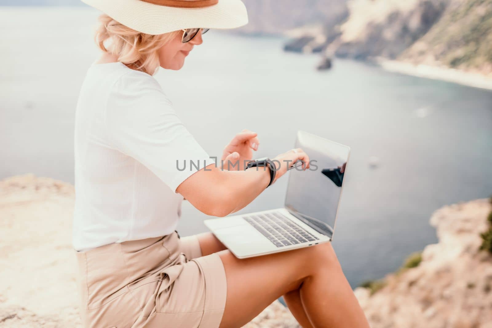 Digital nomad, Business woman working on laptop by the sea. Pretty lady typing on computer by the sea at sunset, makes a business transaction online from a distance. Freelance remote work on vacation