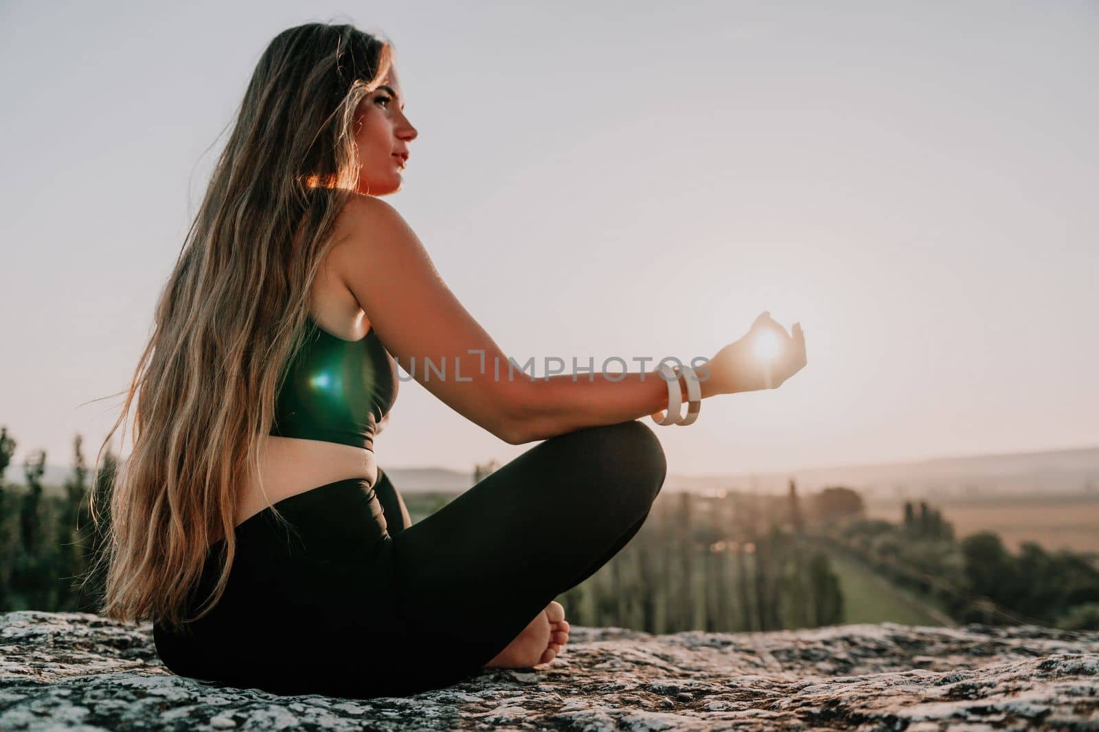 Well looking middle aged woman with long hair, fitness instructor in leggings and tops doing stretching and pilates on the rock near forest. Female fitness yoga routine concept. Healthy lifestyle.