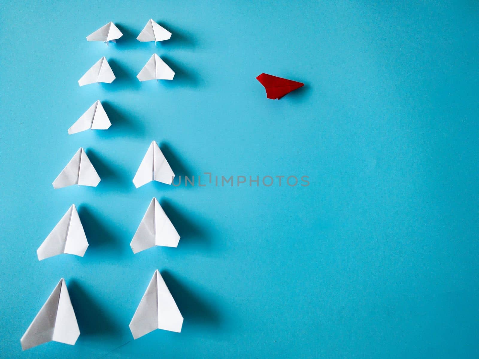 Red airplane origami leaving other white airplanes on blue background with customizable space for text. Leadership skills concept.