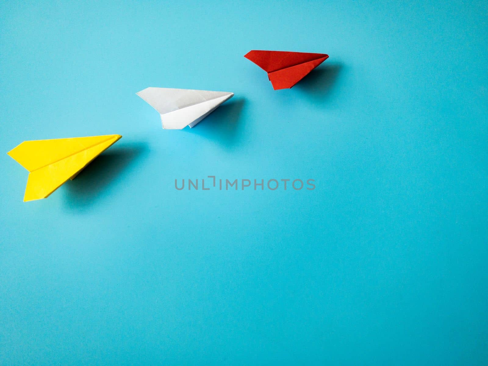 Red paper airplane origami leading white and yellow airplanes on blue background with customizable space for text. Leadership skills concept