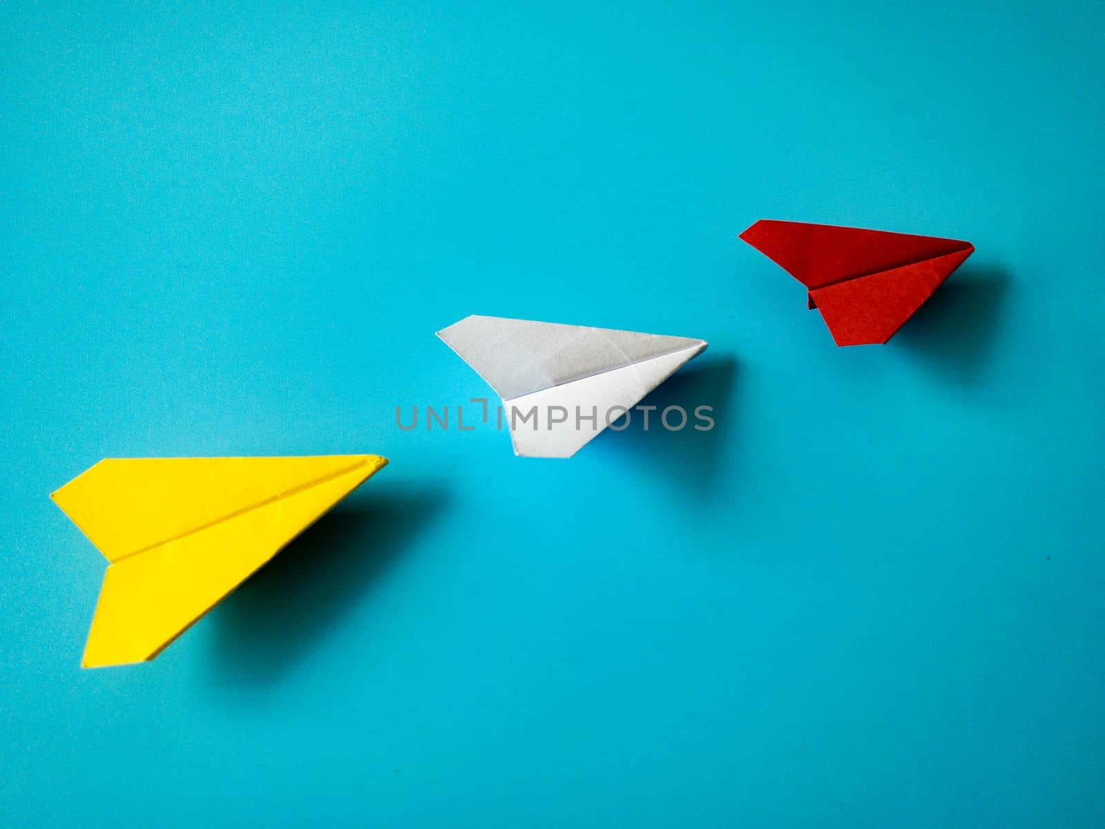 Red paper airplane origami leading white and yellow airplanes on blue background with customizable space for text. Leadership skills concept
