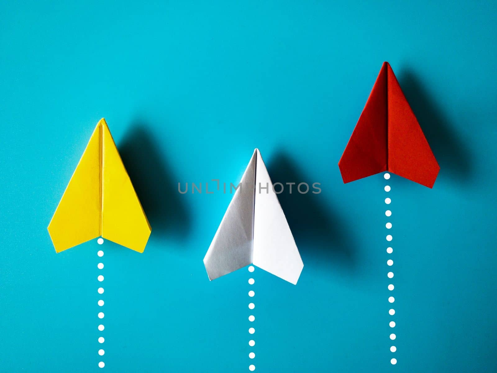 Yellow, white and red paper airplane origami racing to achieve destination on blue background with customizable space for text. Business goals concept.