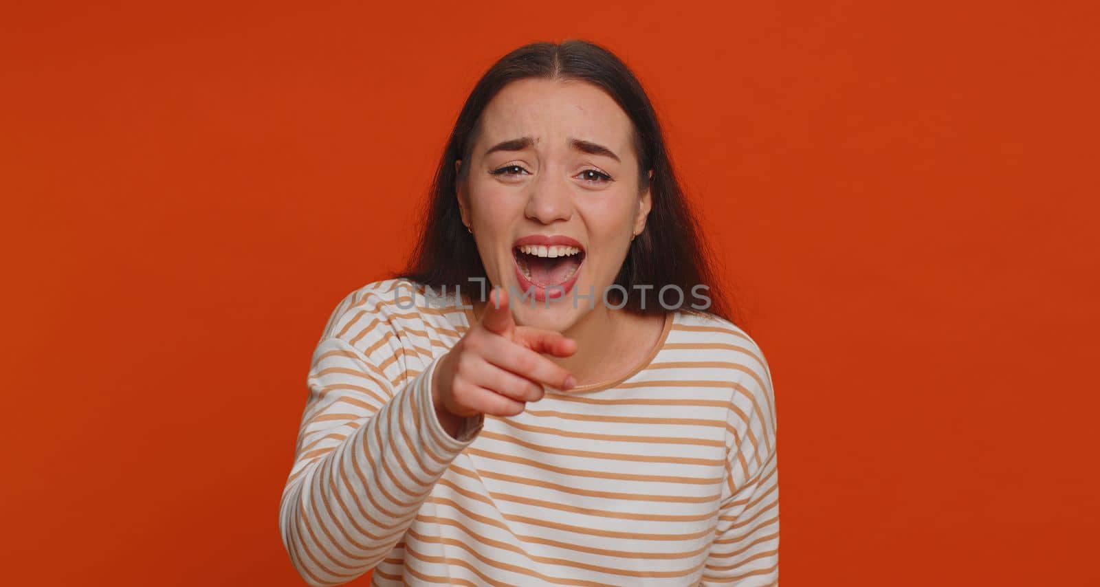 Amused pretty woman pointing finger to camera, laughing out loud, taunting making fun of ridiculous appearance, funny joke anecdote, bullying. Young adult girl isolated alone on red studio background