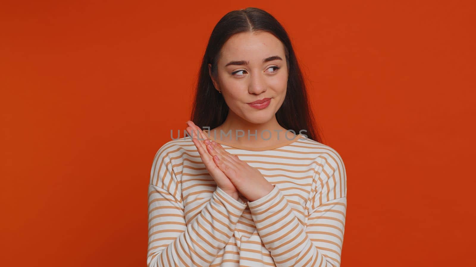 Sneaky cunning pretty woman with tricky face gesticulating and scheming evil plan, thinking over devious villain idea, cheats, revenge, jokes, pranks. Young girl isolated on red studio background