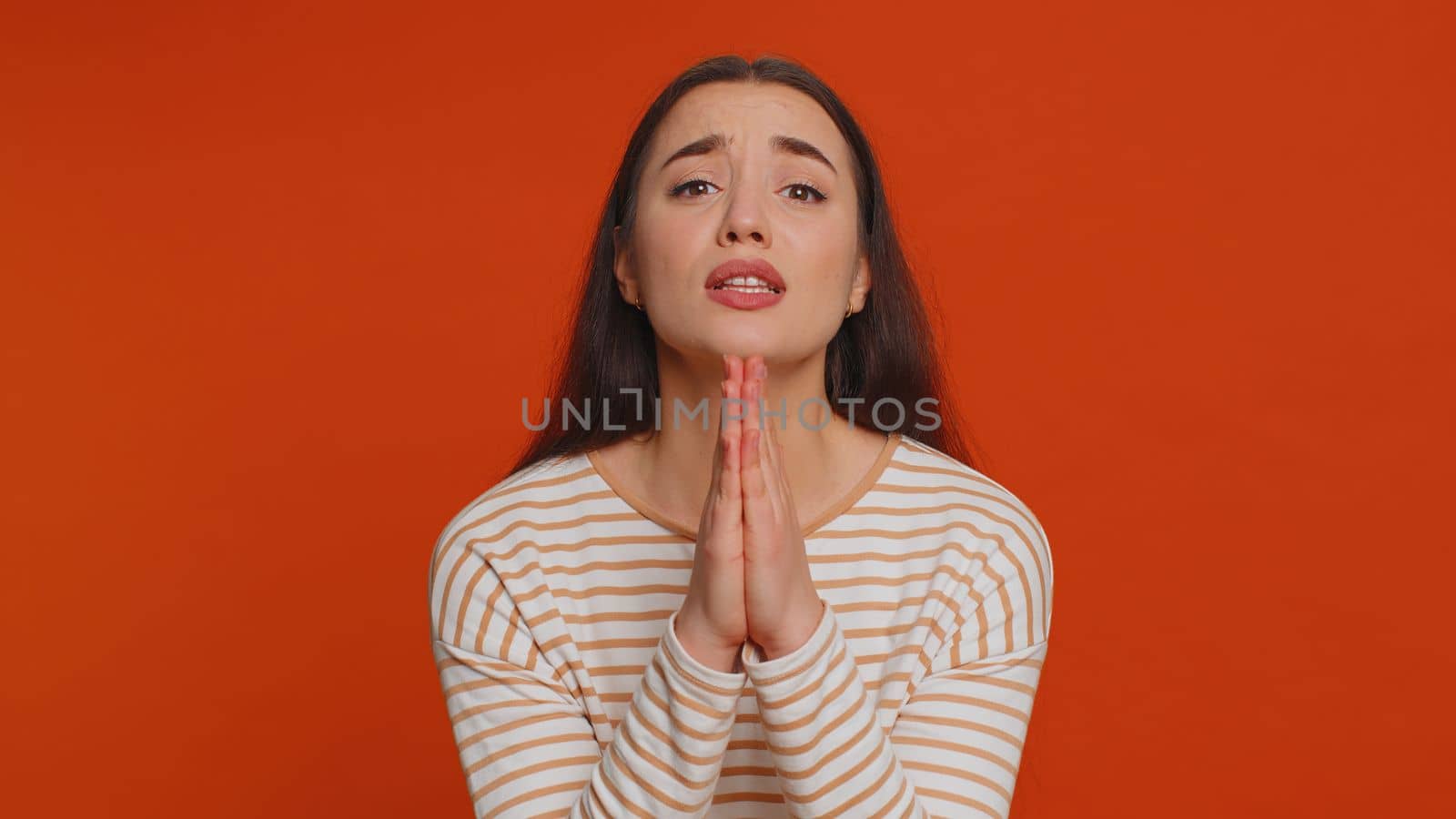 Please, God, forgive me. Young woman sincerely praying to God and looking up with pleading expression, begging apology, beseeching with hopeful face. Millennial girl isolated on red studio background