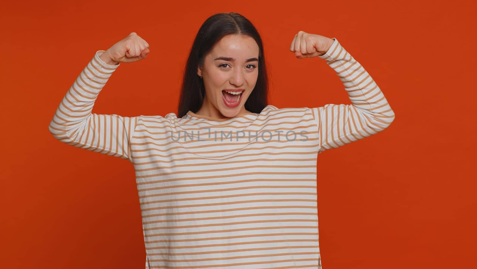 I am strong and independent. Proud success woman showing biceps and looking confident, feeling power strength to fight for rights energy to gain success win. Young adult girl on red studio background
