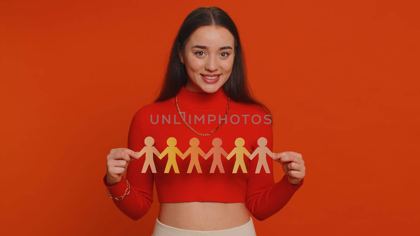 Woman showing multiracial different skin color human shape cut out of paper, concept of teamwork, partnership, community, unity, people support love, against racism. Young girl on red background